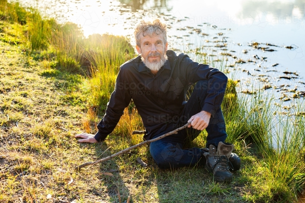 Farmer resting on grass beside dam in paddock - Australian Stock Image