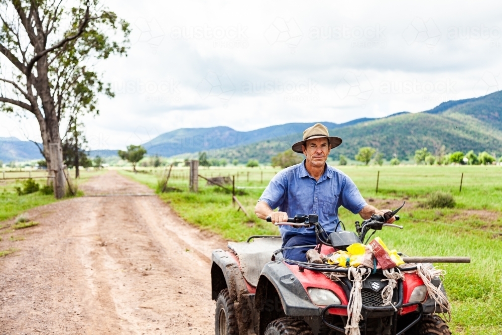 Farmer riding quad bike down farm driveway over cattle grid - Australian Stock Image