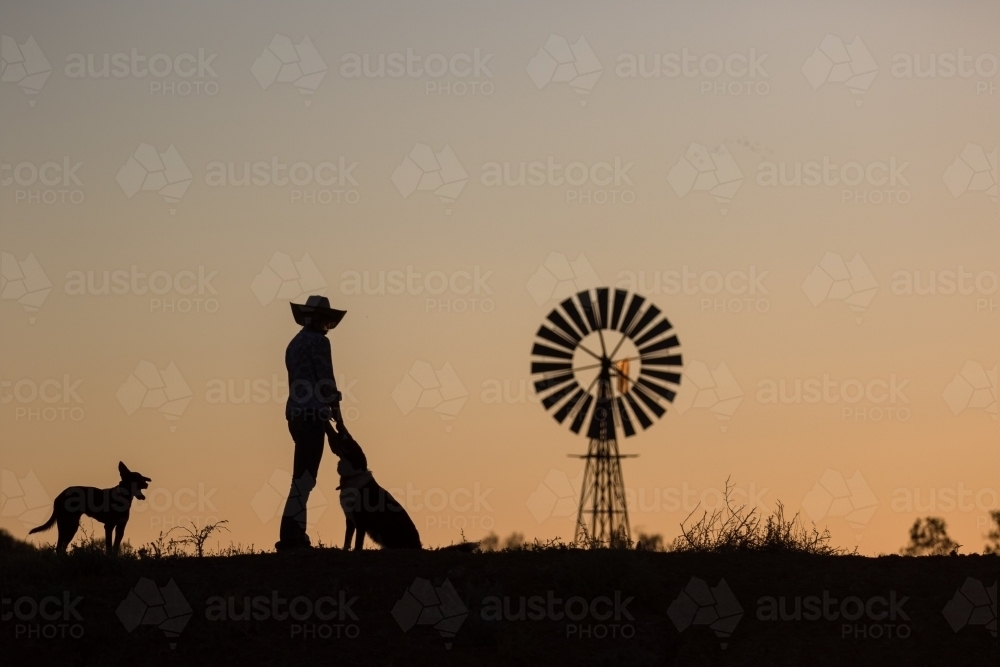 Farmer with dogs and windmill in silhouette - Australian Stock Image