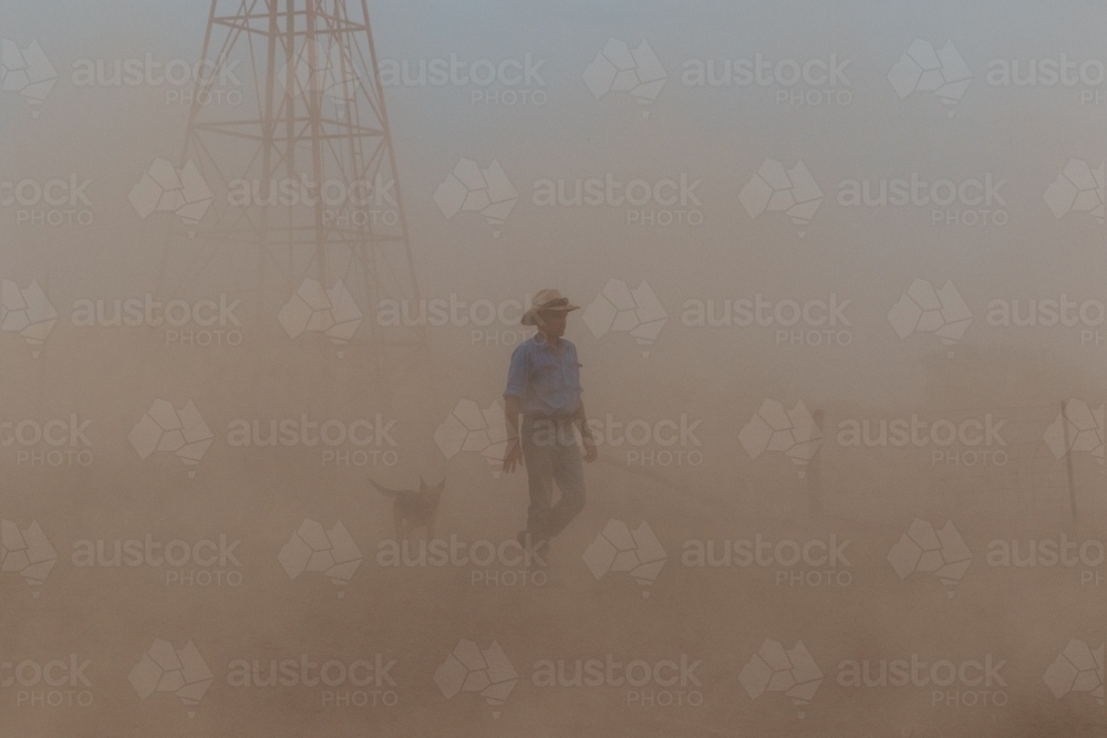 Farmer & working dog in the dust with windmill - Australian Stock Image