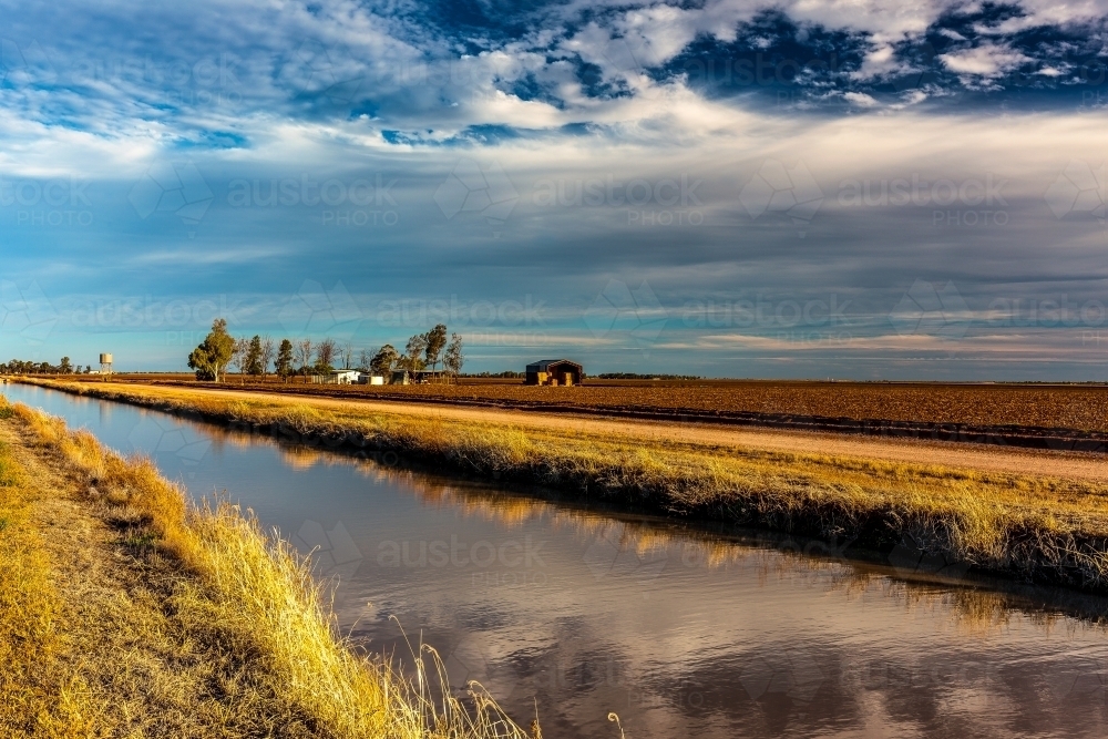 Farmland lining a straight river with farm house in distance - Australian Stock Image