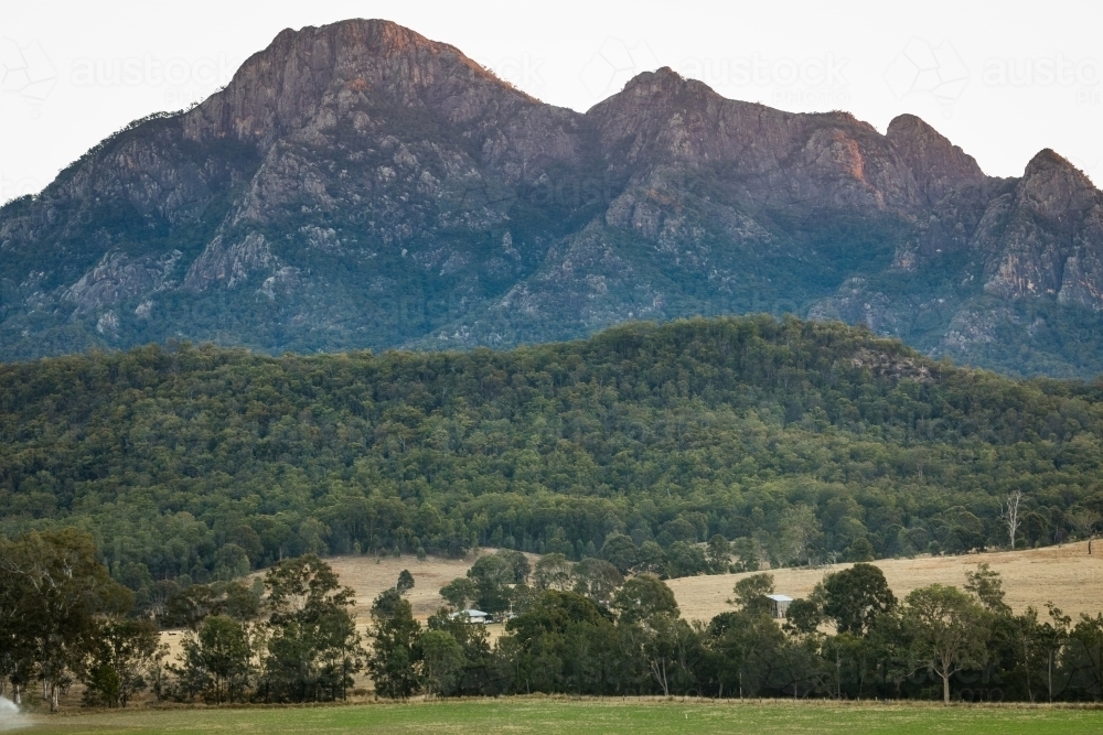 Farmland with a steep rocky mountain rising behind - Australian Stock Image