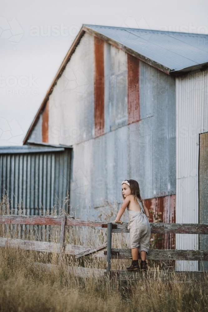 Fashionable young girl climbing a fence in a rural farm setting - Australian Stock Image