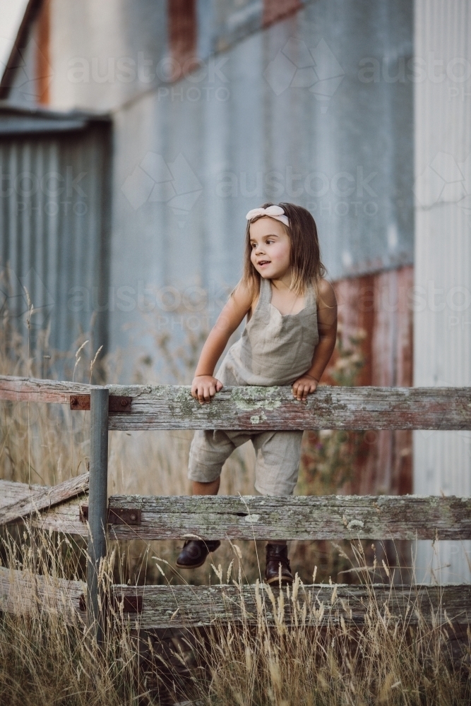 Fashionable young girl climbing a fence in a rural farm setting - Australian Stock Image