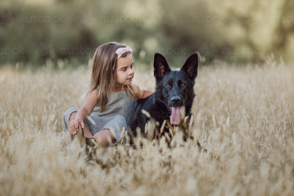 Fashionable young girl, patting a black dog in a farm setting - Australian Stock Image