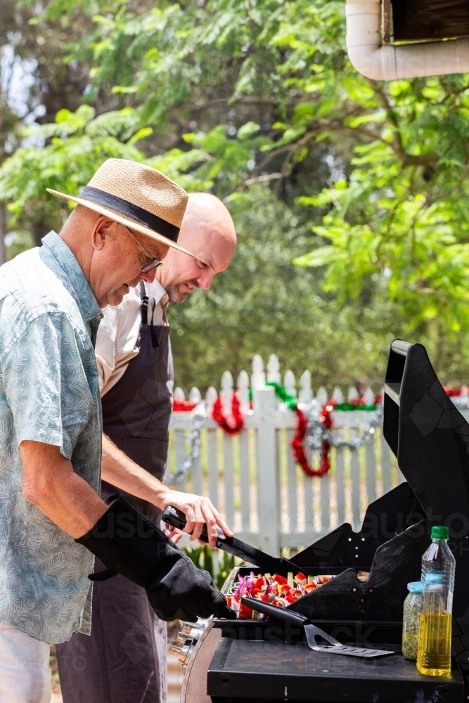 Father and adult son cooking bbq lunch together in backyard of country home - Australian Stock Image