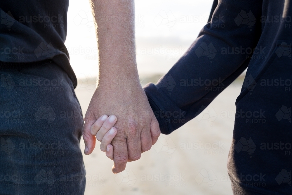 Father and child holding hands on beach - Australian Stock Image