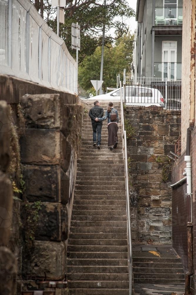Father and daughter holding hands climbing up steps to street - Australian Stock Image