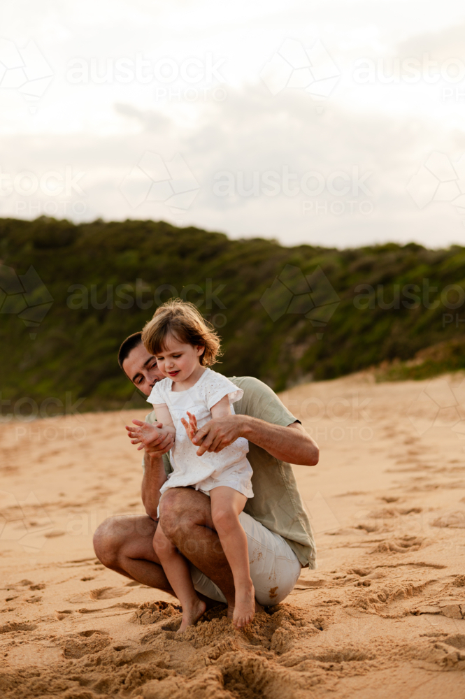 Father and daughter playing together at sunset on a sandy beach - Australian Stock Image