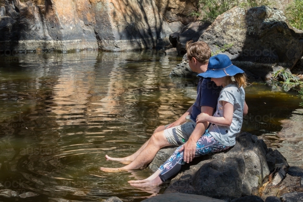 Father and daughter sit near a waterhole in inland Australia - Australian Stock Image