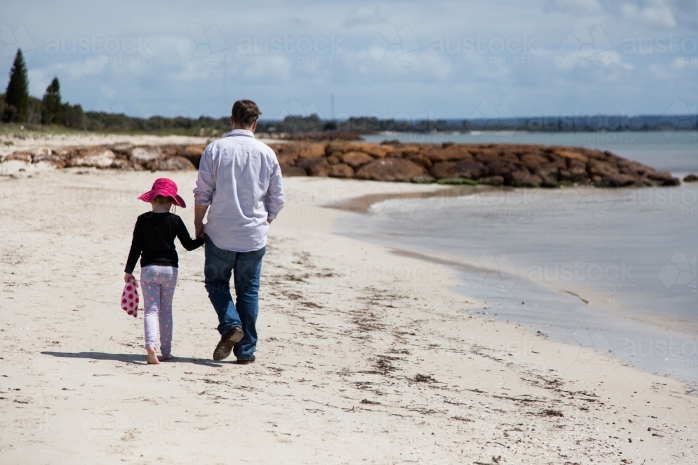 Father and daughter walk hand in hand along a beach - Australian Stock Image