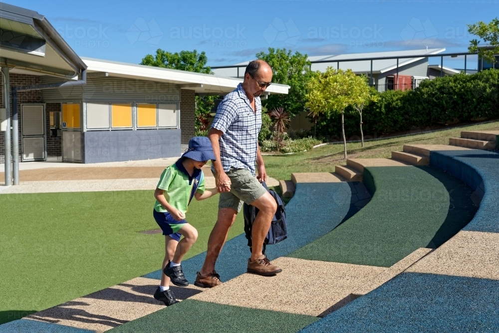 Father and daughter walking hand in hand up the steps at school - Australian Stock Image