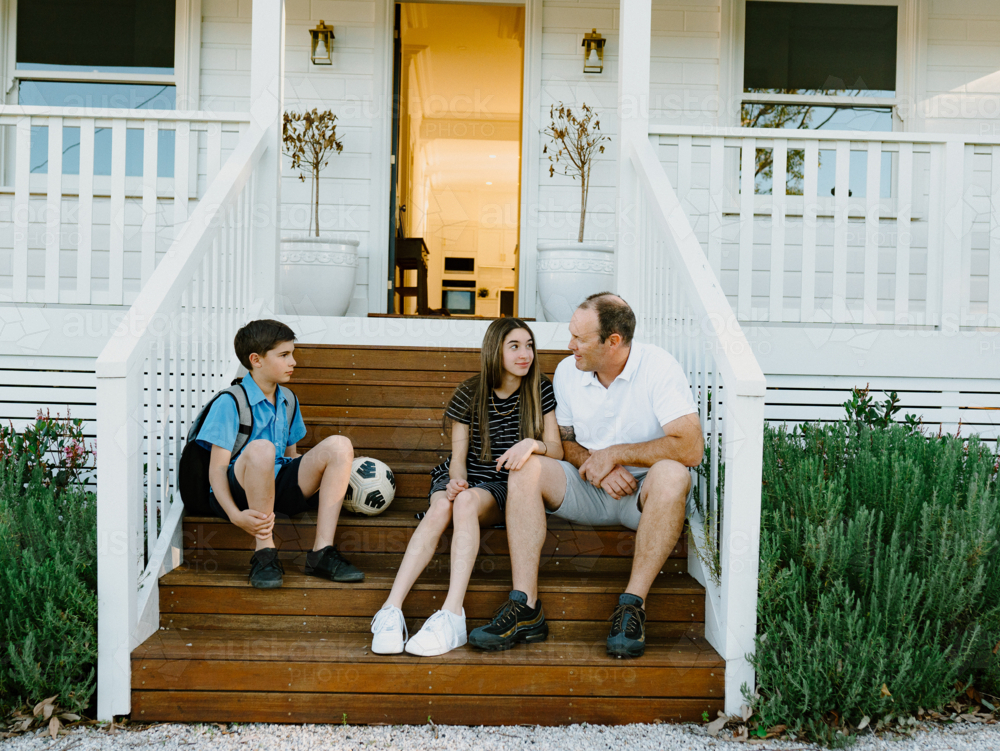 Father and his children sitting on the porch wooden steps. - Australian Stock Image