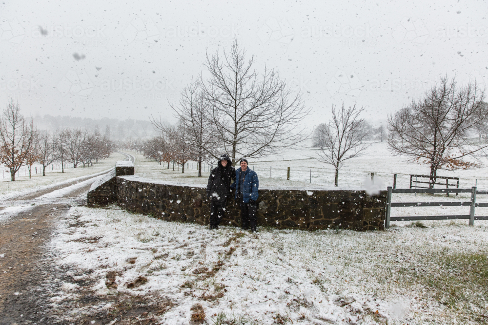 Father and son against brick wall of driveway smiling in snow - Australian Stock Image