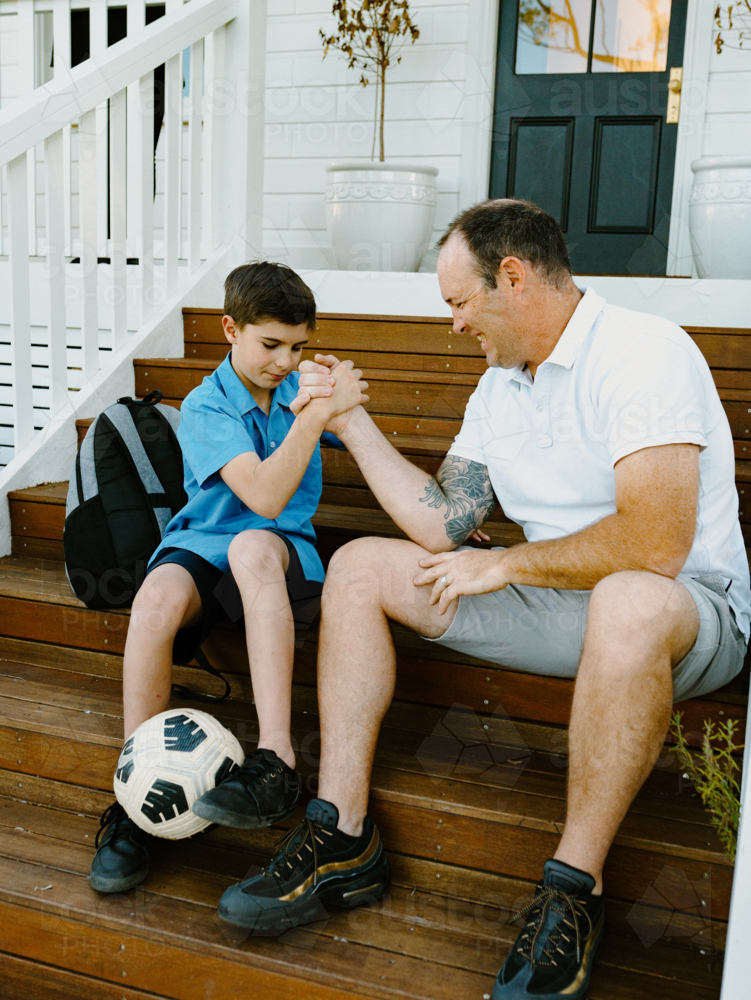 Father and son doing arm wrestling while sitting on the steps of their house. - Australian Stock Image