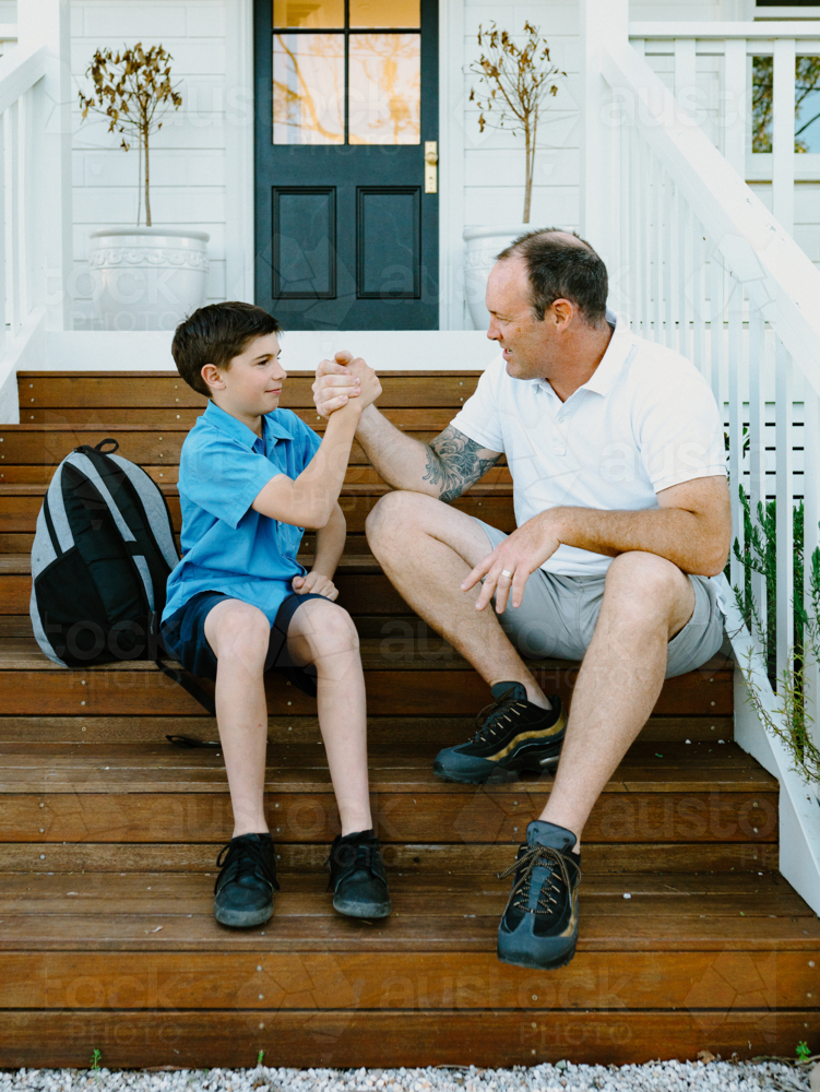 Father and son doing arm wrestling while sitting on the steps of their house. - Australian Stock Image
