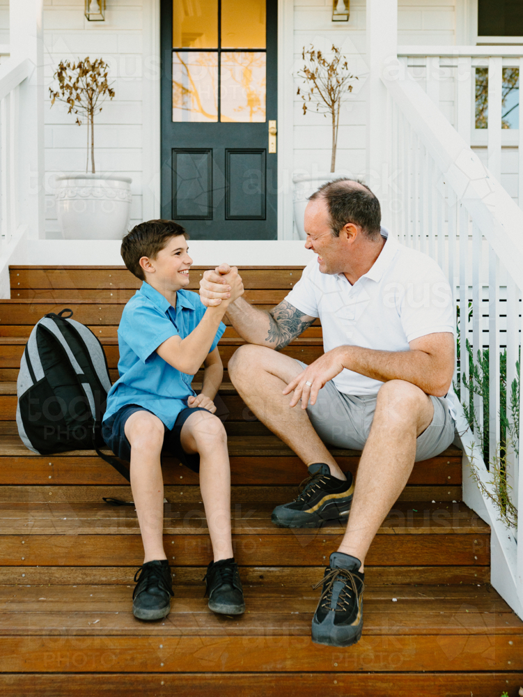Father and son doing arm wrestling while sitting on the steps of their house. - Australian Stock Image