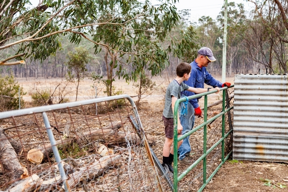Father and son doing temporary repairs on a fence using old gates - Australian Stock Image