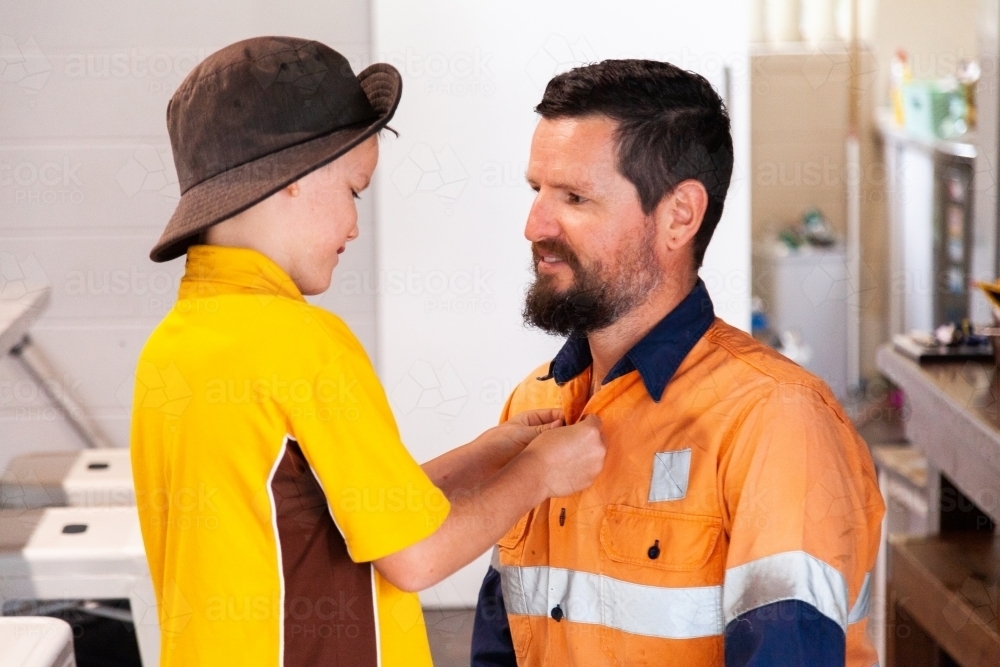Father and son helping each other do up shirt buttons before work and school - Australian Stock Image