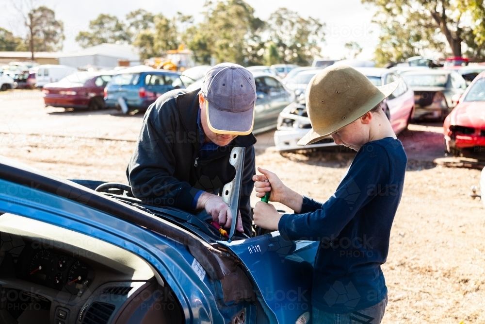 Father and son in wreckers pulling apart smashed car for parts - Australian Stock Image
