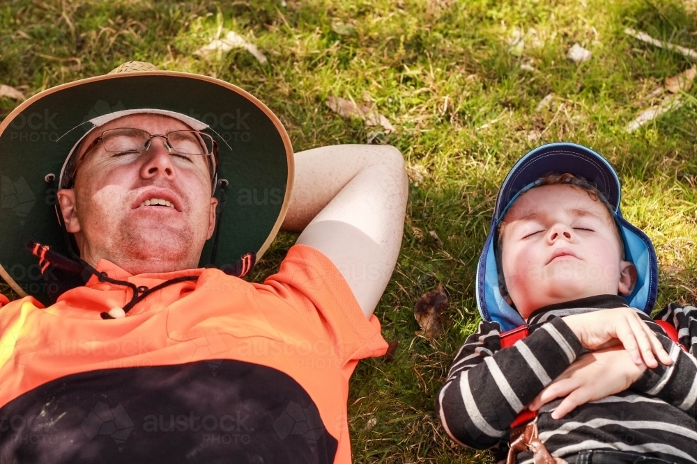 Father and son lying on grass sleeping - Australian Stock Image