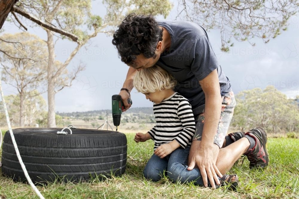 Father and son making a tyre swing in country backyard - Australian Stock Image