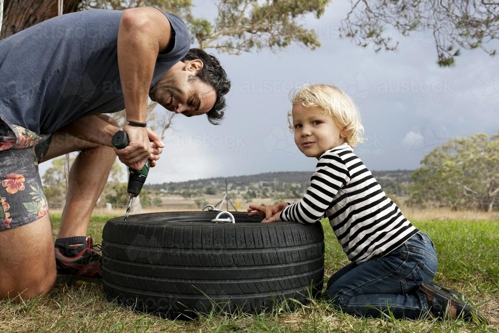 Father and son making a tyre swing in country backyard - Australian Stock Image