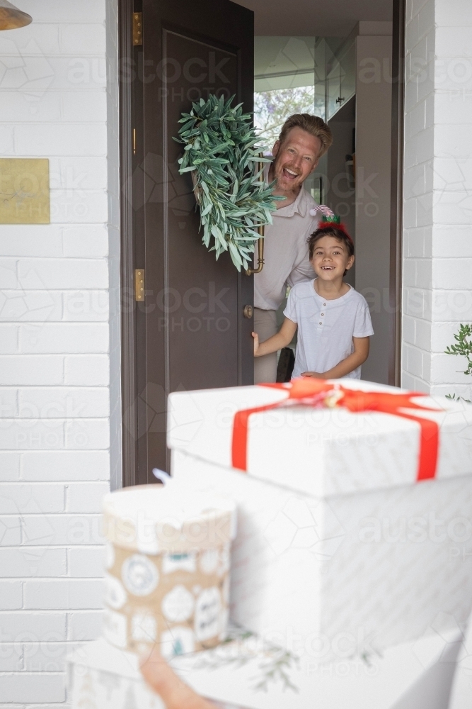 Father and son opening door with wreath to see Christmas presents - Australian Stock Image