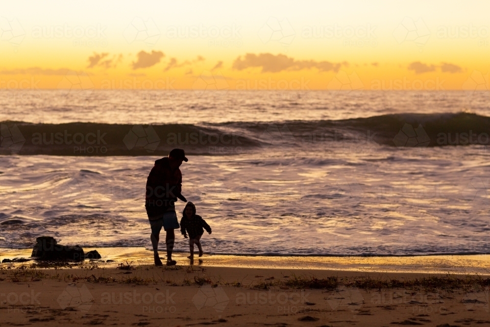 Father and son play at the water's edge at sunset - Australian Stock Image