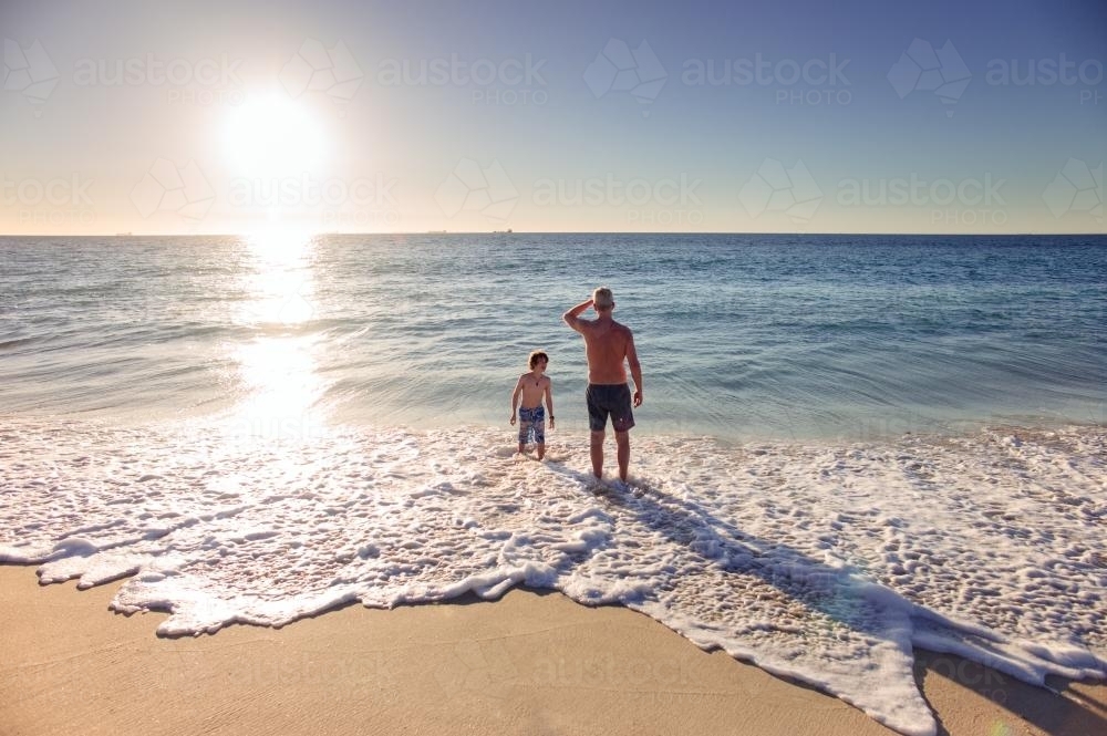 Father and son playing in the waves at the beach at sunset in summer - Australian Stock Image