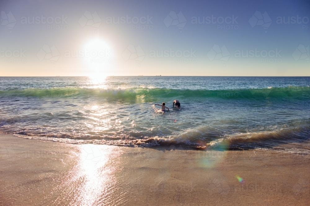 Father and son playing in the waves at the beach at sunset in summer - Australian Stock Image