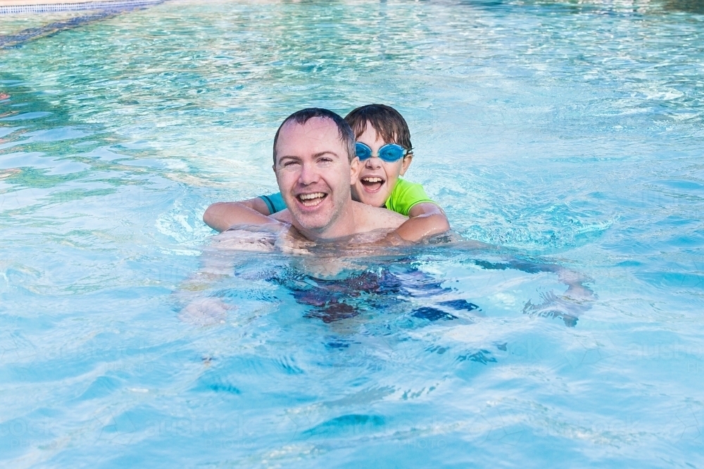 Father and son playing together in swimming pool laughing having fun - Australian Stock Image