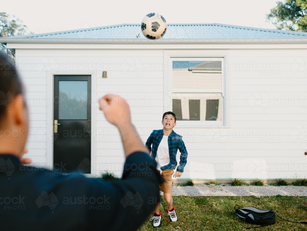 Father and son playing with a soccer ball outside the house. - Australian Stock Image