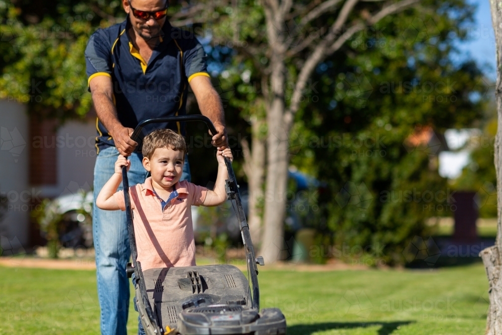 Father and son pushing lawnmower in suburban yard - Australian Stock Image