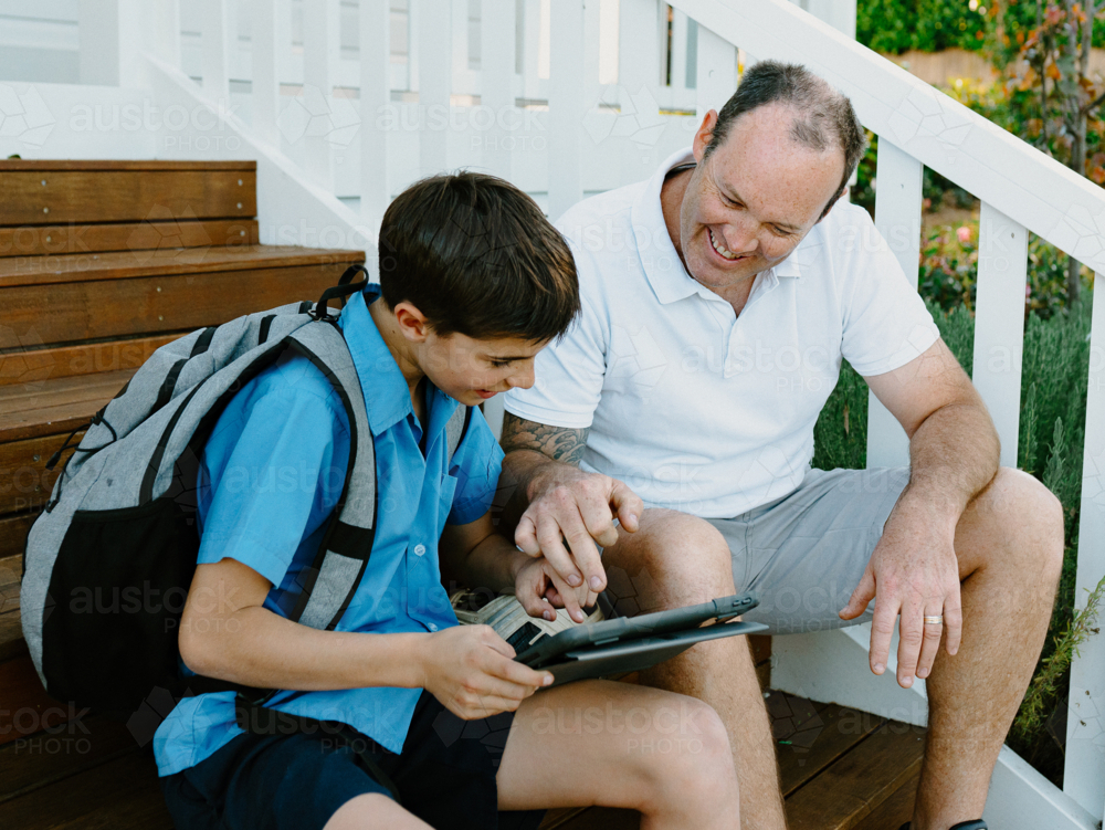 Father and son sitting on the steps using an iPad. - Australian Stock Image