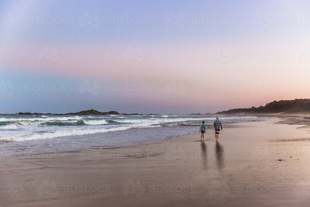 Father and son walking on beach at sunset from behind - Australian Stock Image