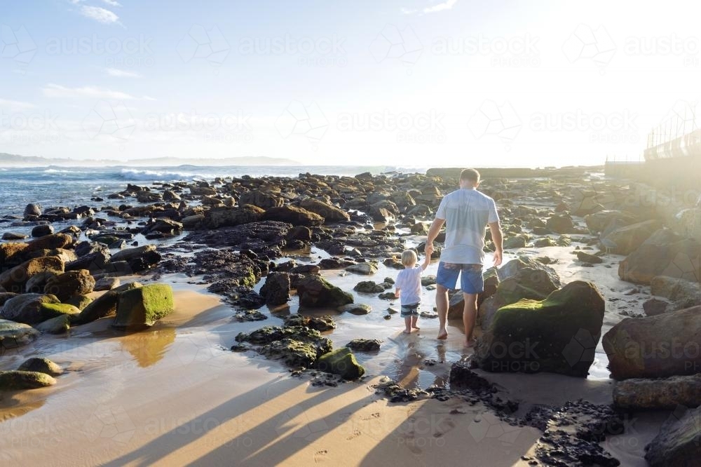 Father and son walking through the rock pools at sunrise - Australian Stock Image