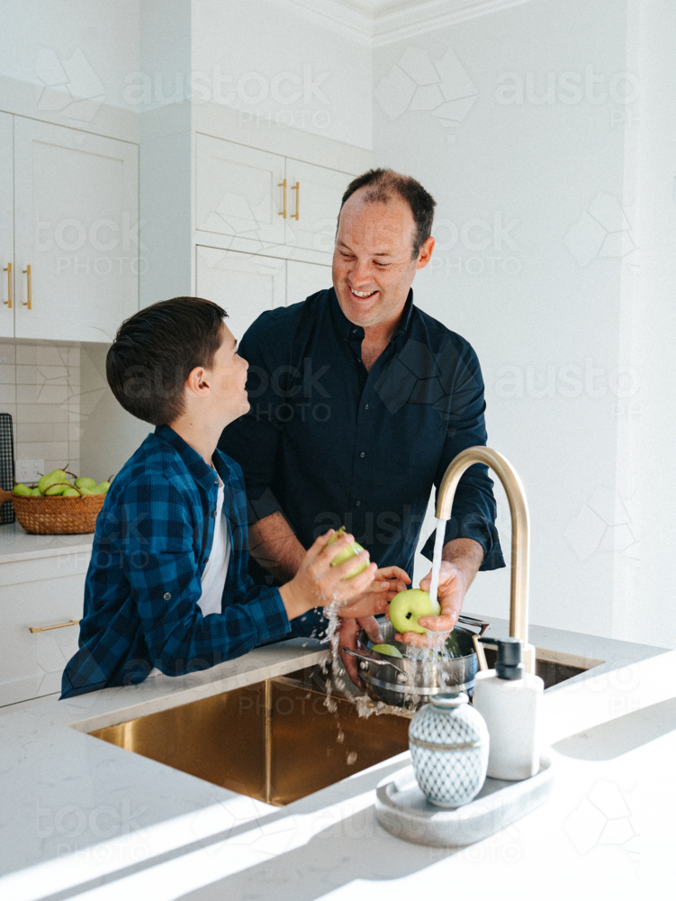 Father and son washing apples in the kitchen sink. - Australian Stock Image