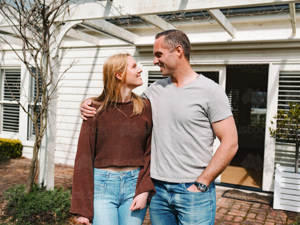 Father and teenage daughter stands closely looking at each other smiling in the patio on a sunny day - Australian Stock Image