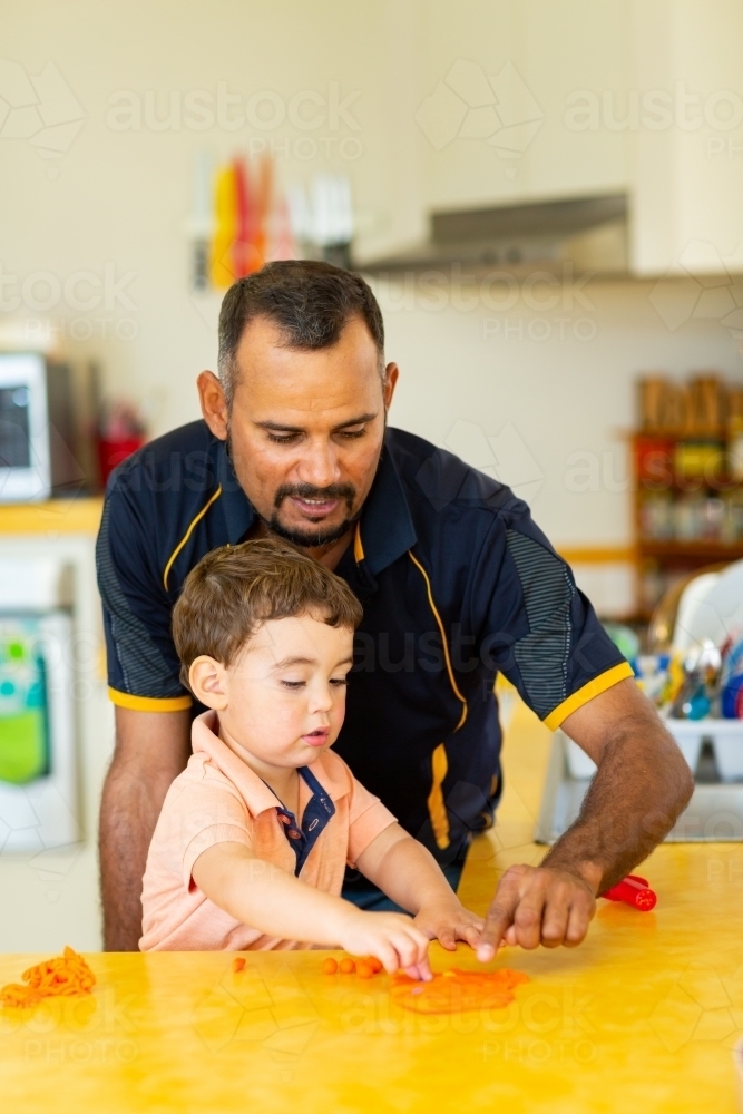 Father and toddler son playing with coloured dough in kitchen - Australian Stock Image