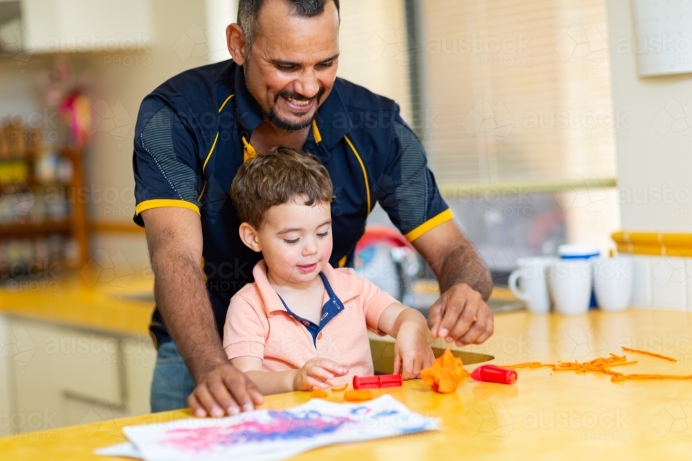 Father and toddler son playing with coloured dough in kitchen - Australian Stock Image