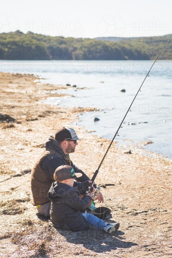 Father and young boy together fishing on the banks of a river - Australian Stock Image