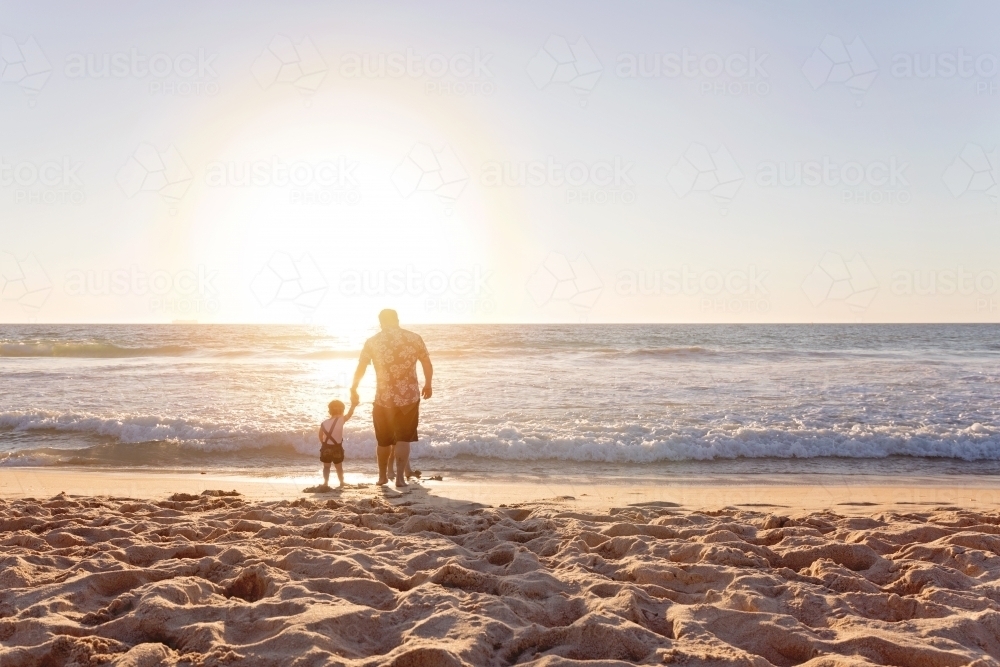 Father And Young Child Holding Hands On The Beach At Sunset - Australian Stock Image