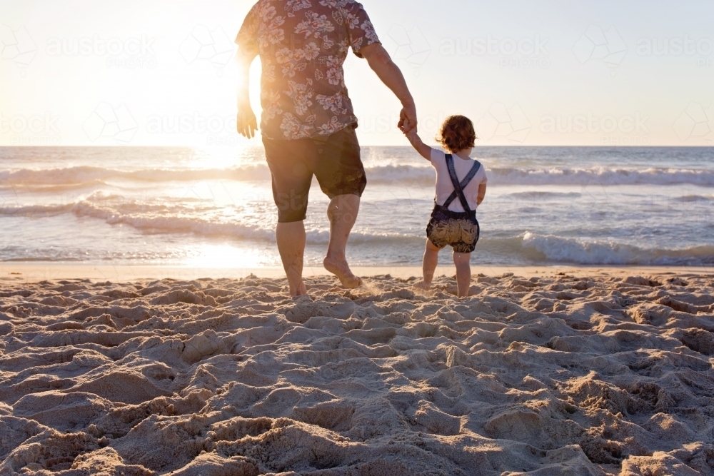 Father And Young Child Holding Hands On The Beach At Sunset - Australian Stock Image