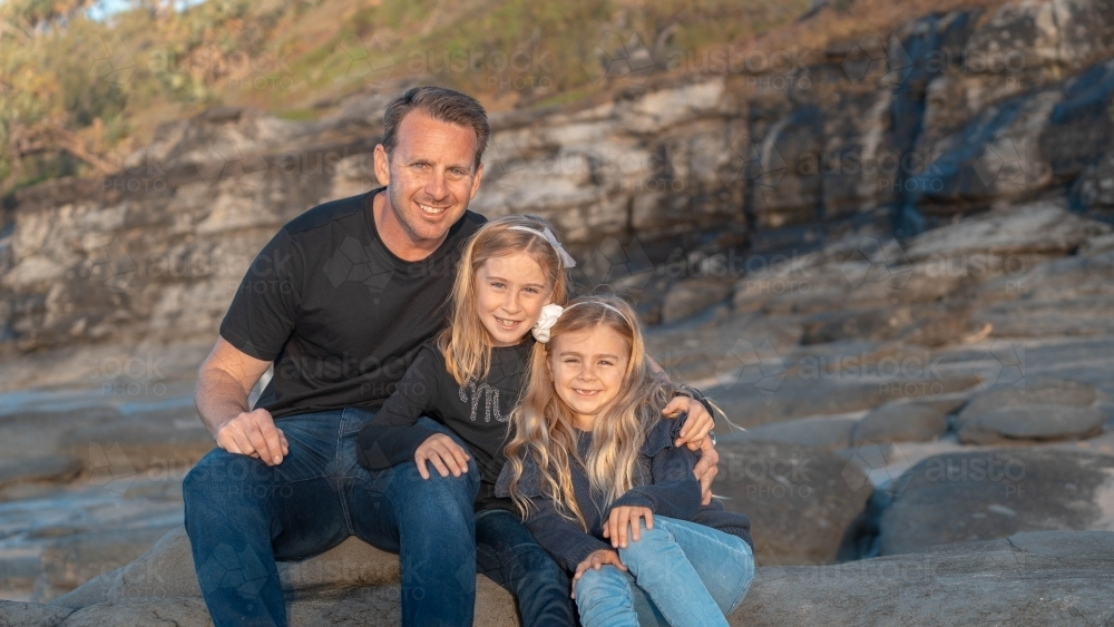Father and young daughters sitting on a large boulder - Australian Stock Image