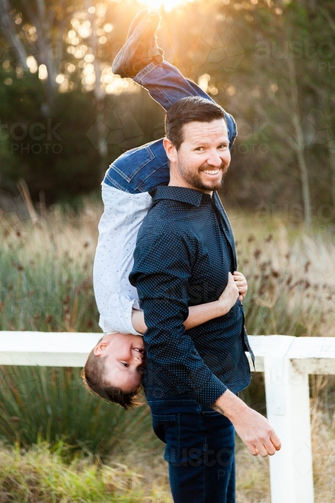 Father being silly with child holding son upside down over shoulder - Australian Stock Image