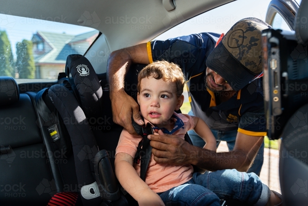 father buckling child into car seat restraint - Australian Stock Image