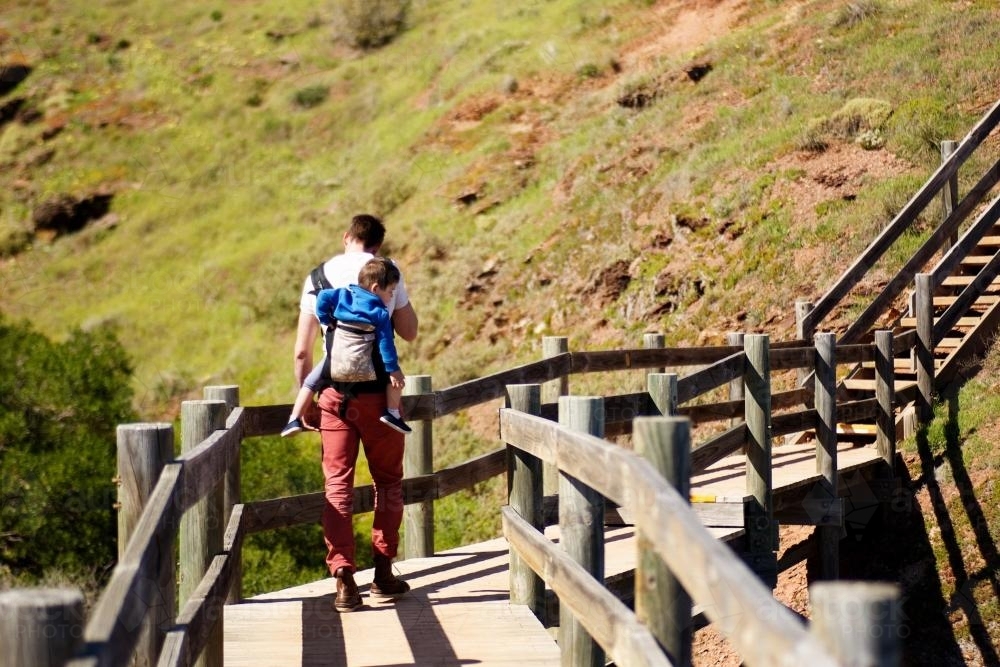 Father carrying a child on his back walking - Australian Stock Image