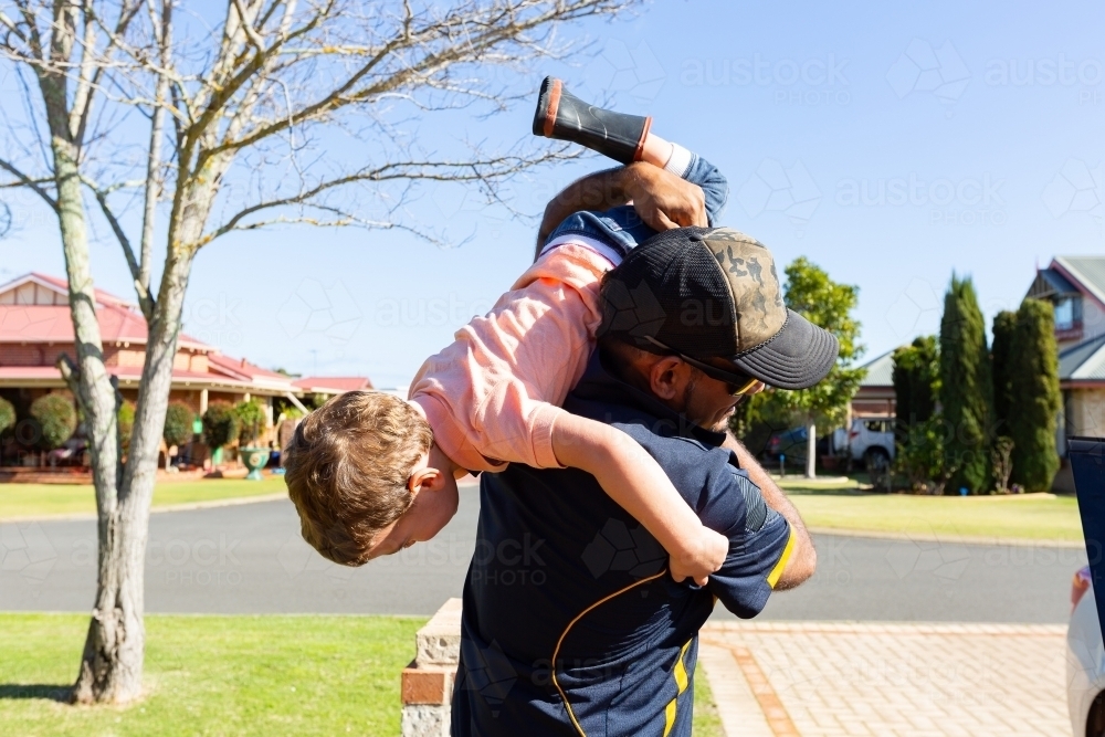 father carrying child upside down over shoulder - Australian Stock Image