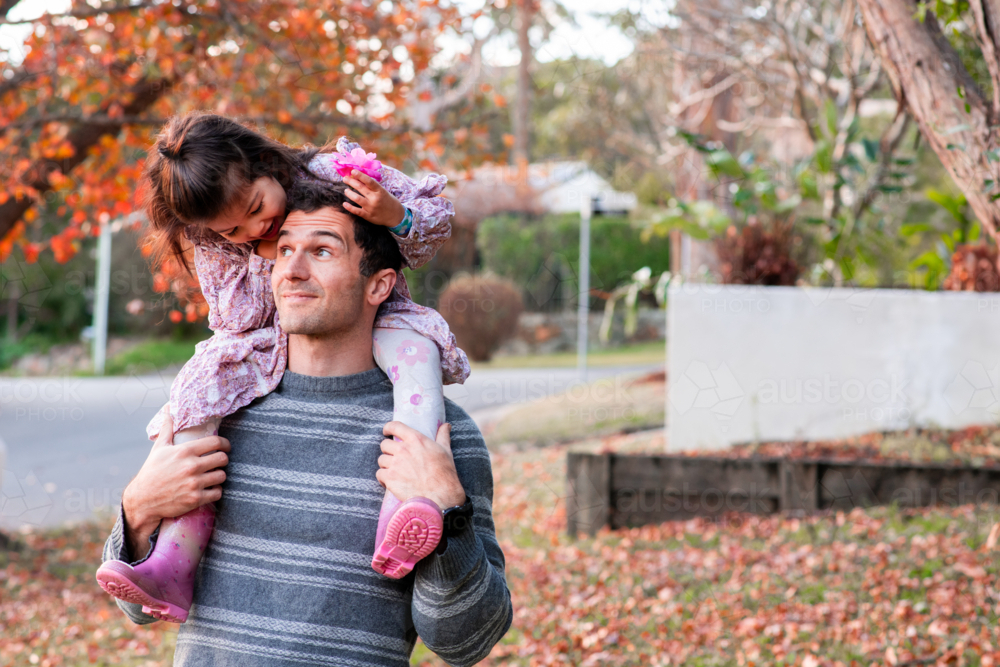 Father Carrying Daughter on Shoulders During Autumn Walk in Suburban Street - Australian Stock Image